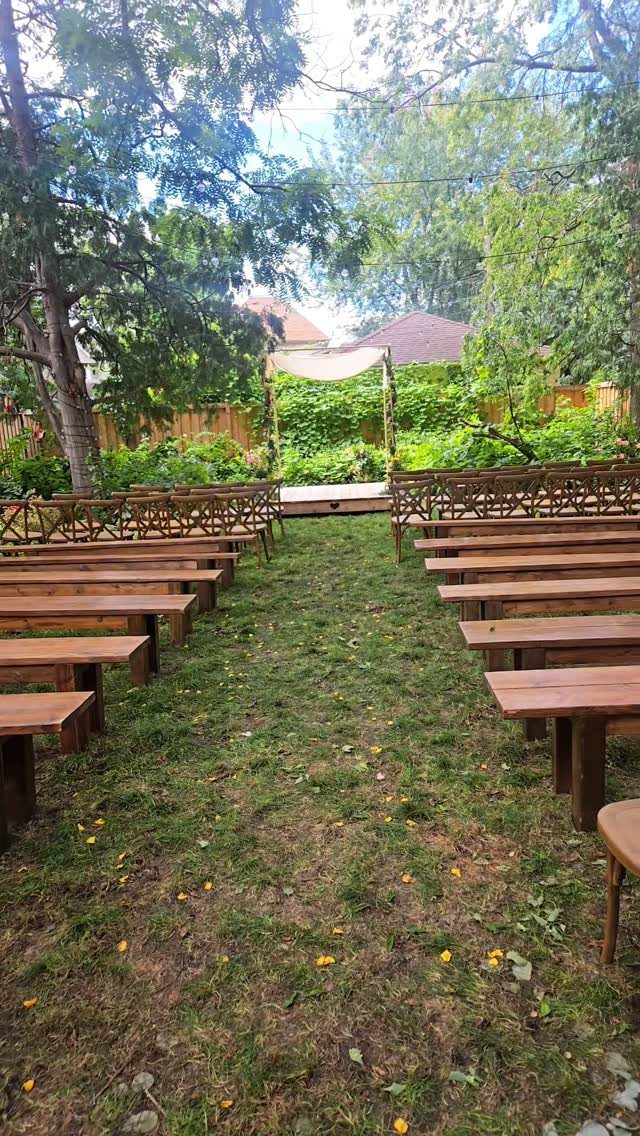 Wooden benches arranged in rows on a lawn leading to a white canopy arch.