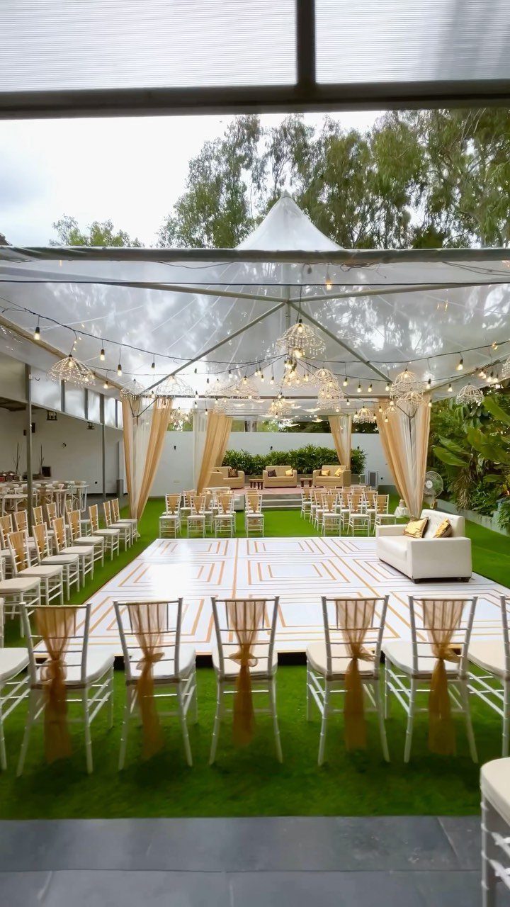 A wedding reception setup under a clear marquee tent with a dance floor and chairs.