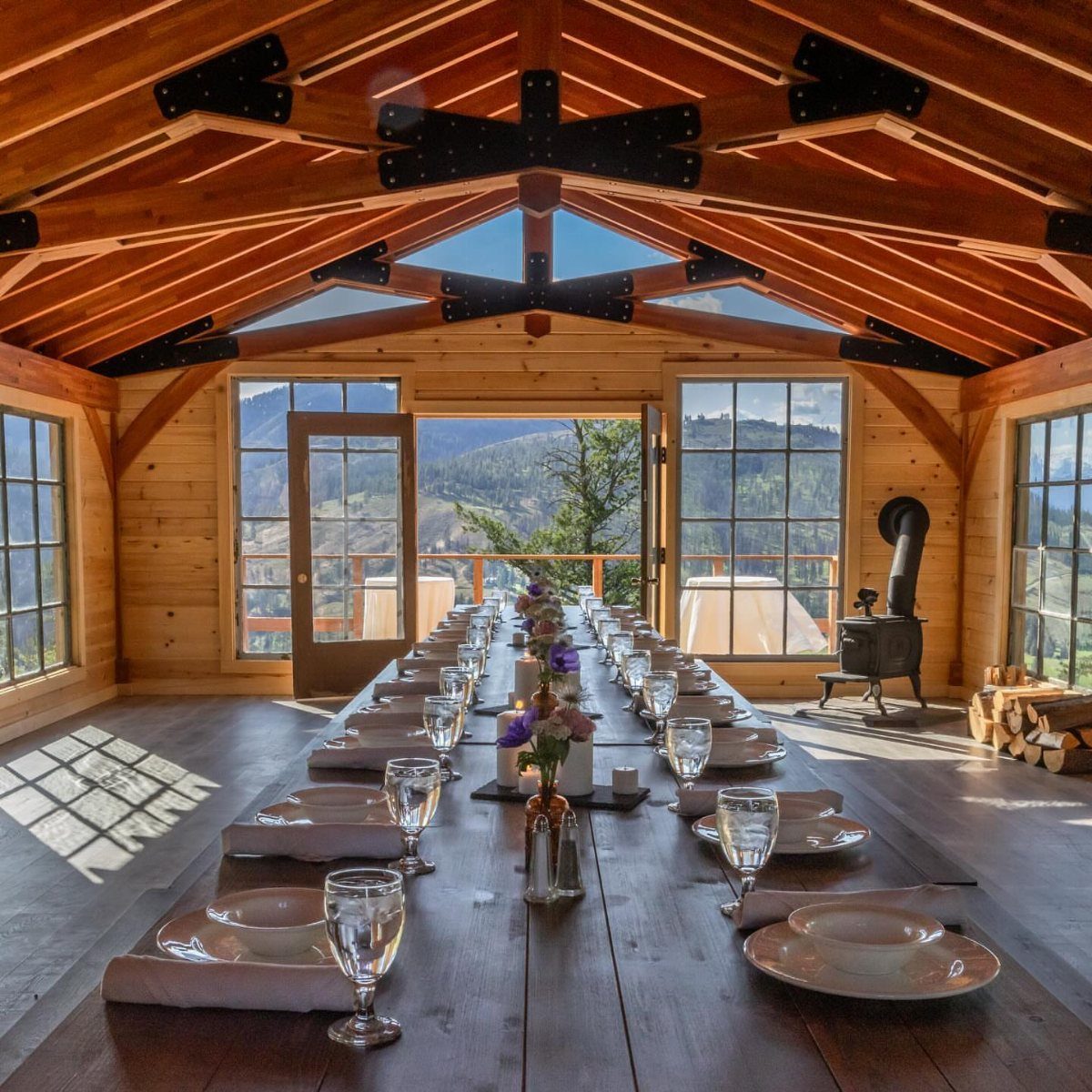 A long dining table set with white plates and glassware inside a rustic wooden lodge.