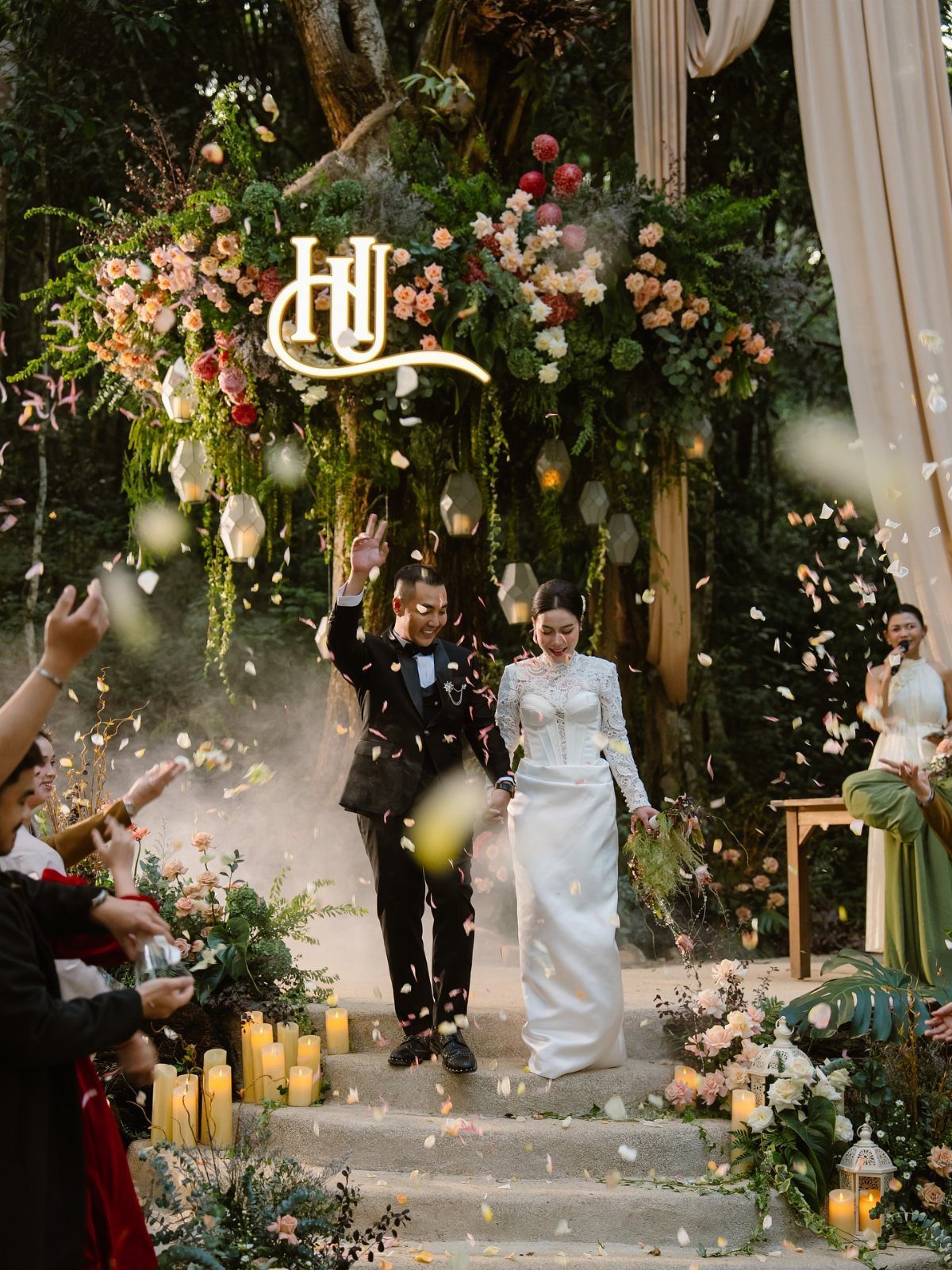 Twilight Forest Wedding Ideas: 10 Concepts for 2026 7 A bride and groom walking through a forest wedding ceremony with falling flower petals.