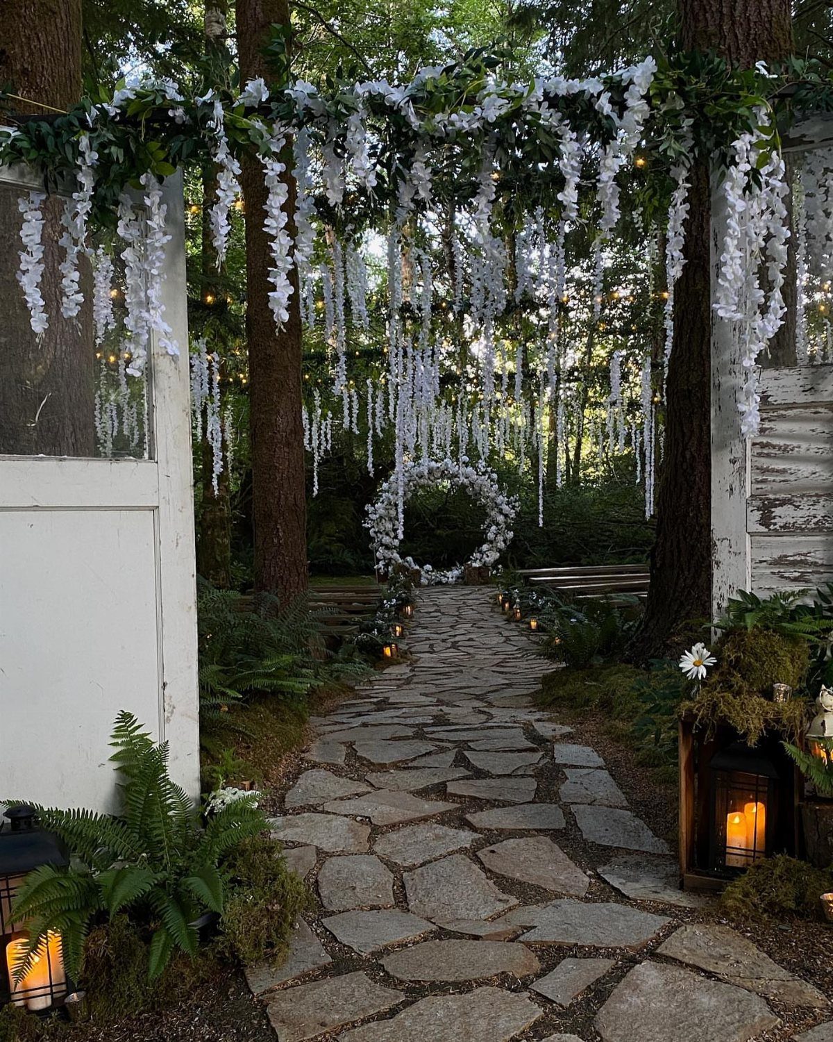 Twilight Forest Wedding Ideas: 10 Concepts for 2026 6 Stone pathway leading through a forest toward a white floral archway and hanging white flowers.