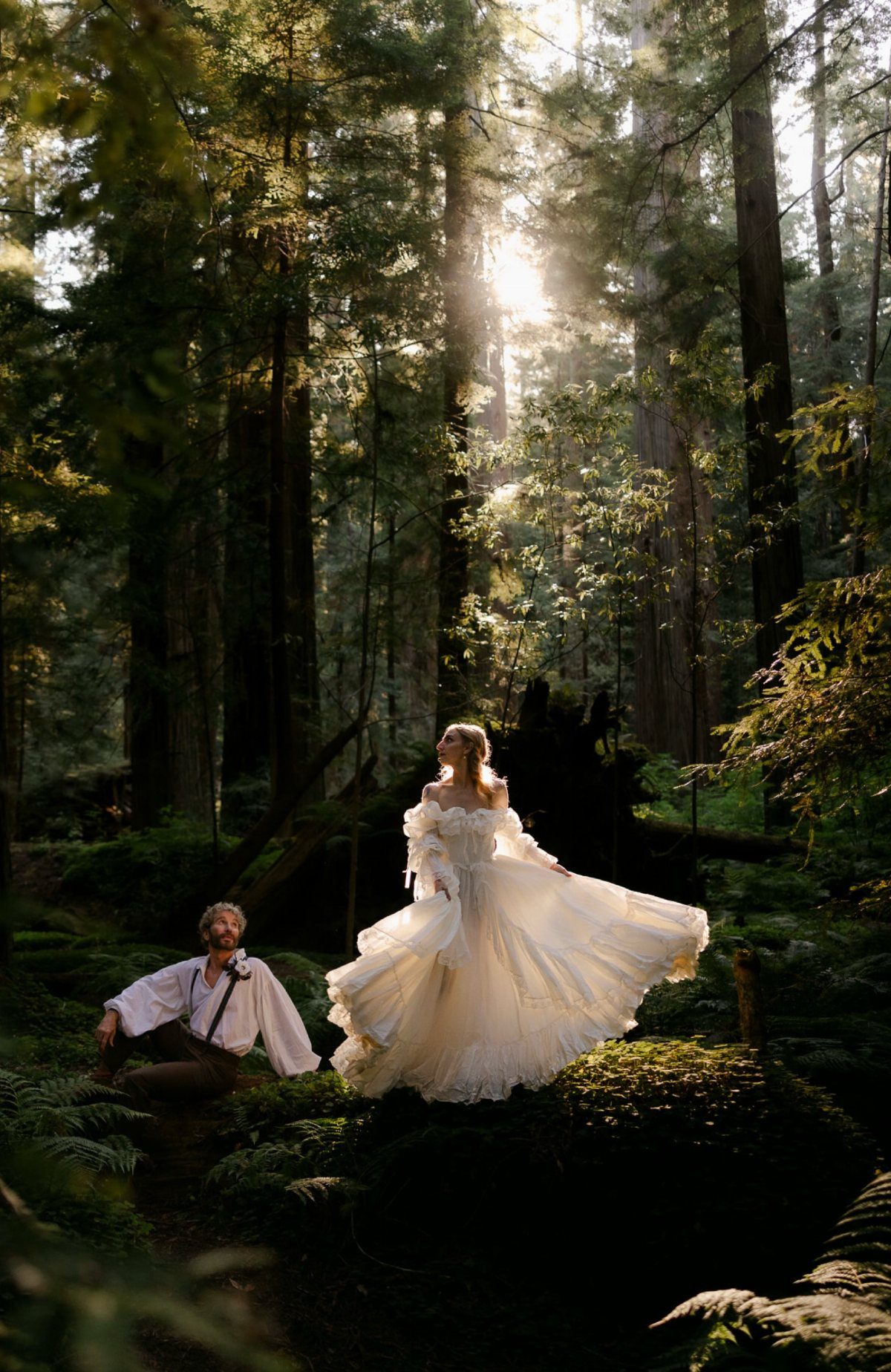 Twilight Forest Wedding Ideas: 10 Concepts for 2026 5 A bride and groom posing in a sunlit, misty forest with tall trees and ferns.