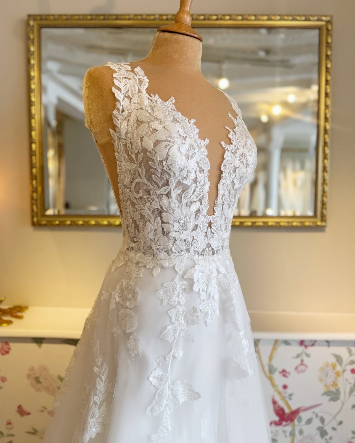 A white wedding dress with floral lace appliqués displayed on a mannequin.
