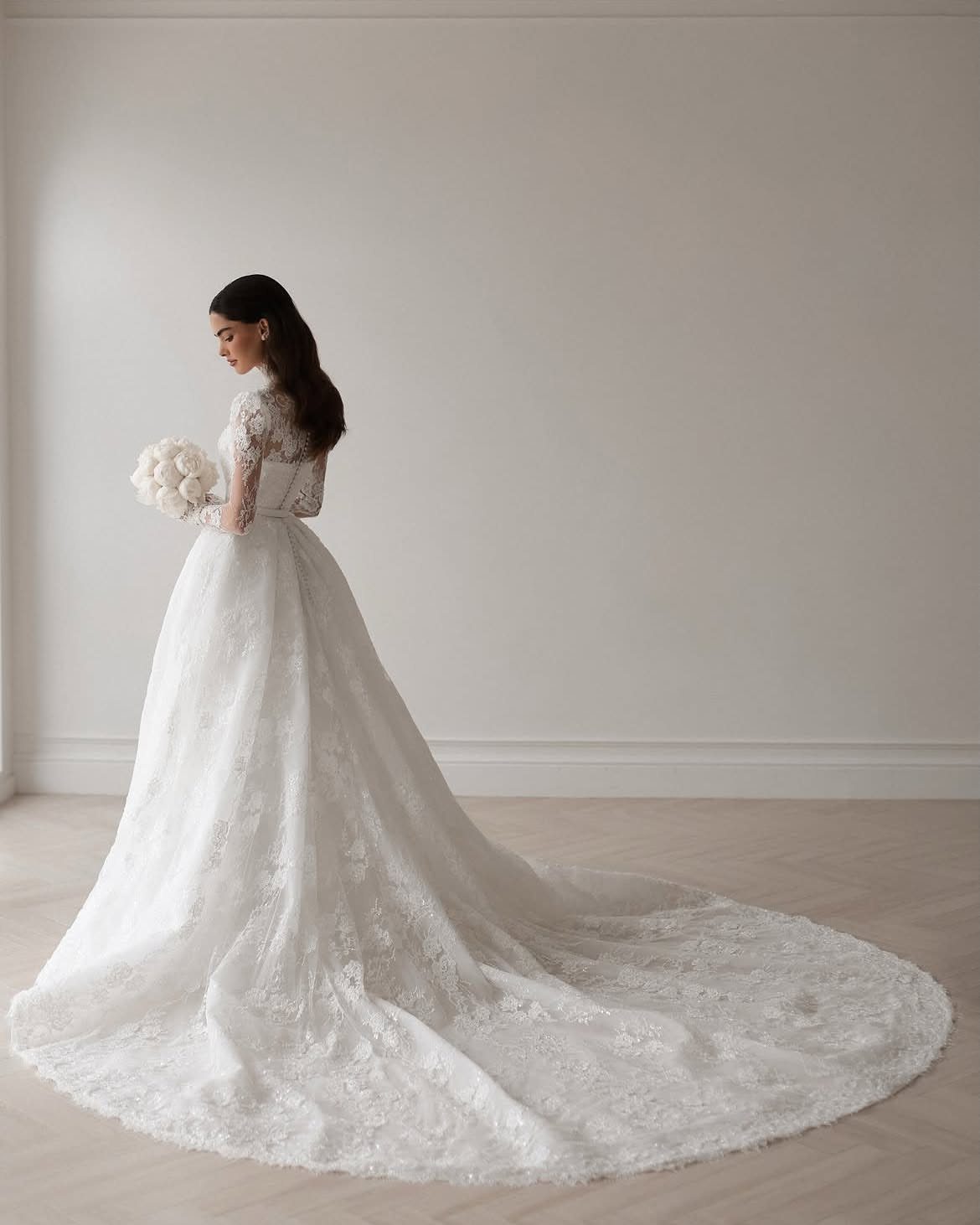 A woman in a long-sleeved white lace wedding gown with a long train.