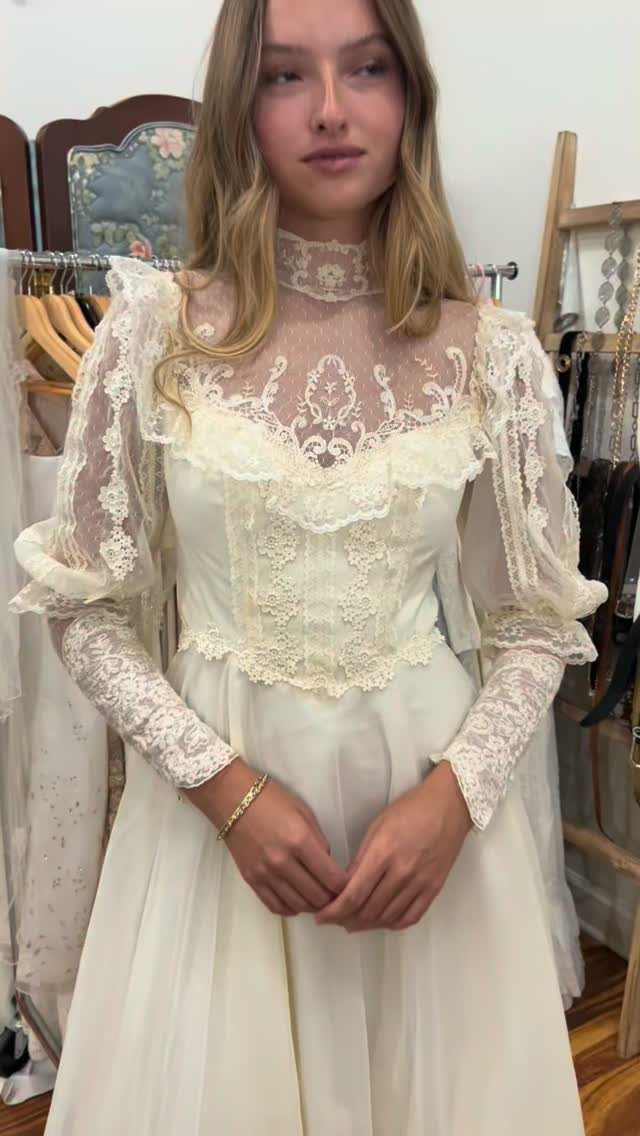 A young woman wearing a vintage cream lace gown with a high neck and long sleeves.