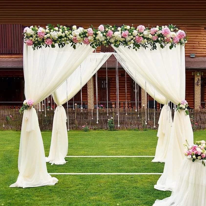 A white wedding arbor decorated with pink and white flowers and draped with flowing white fabric.