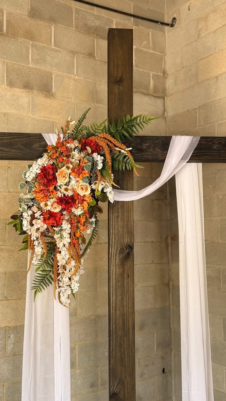 A wooden cross decorated with vibrant orange and white flowers and draped with white fabric.