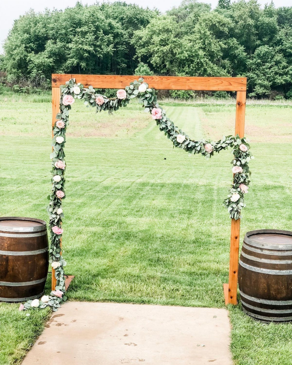A wooden wedding arch decorated with green leafy garlands and pink roses on a grassy field.