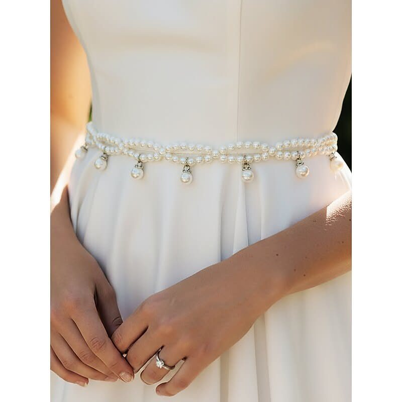 A white wedding dress featuring a decorative pearl belt with hanging pearl droplets around the waist.