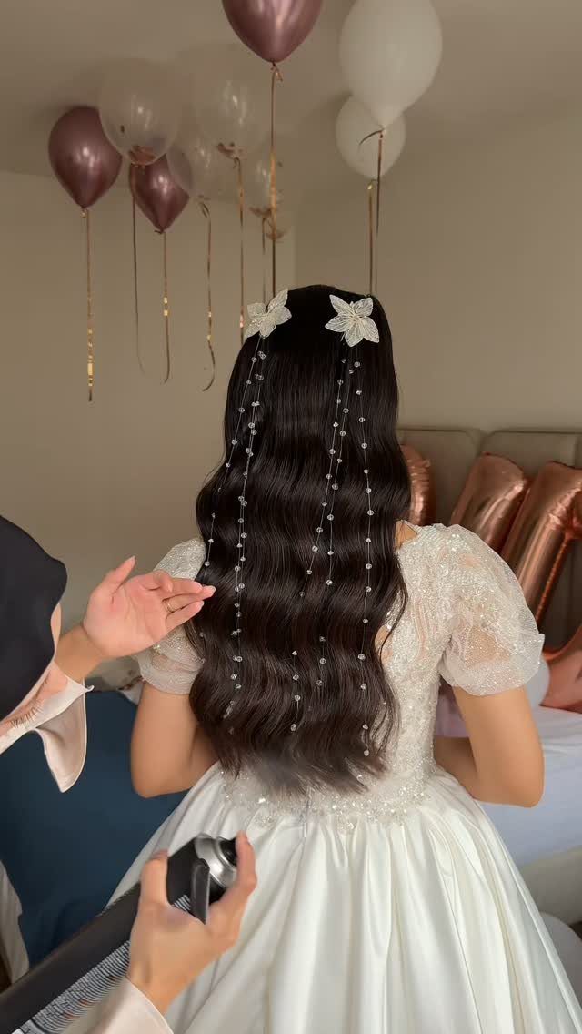 Long dark wavy hair decorated with white floral hair accessories and hanging pearl strands.