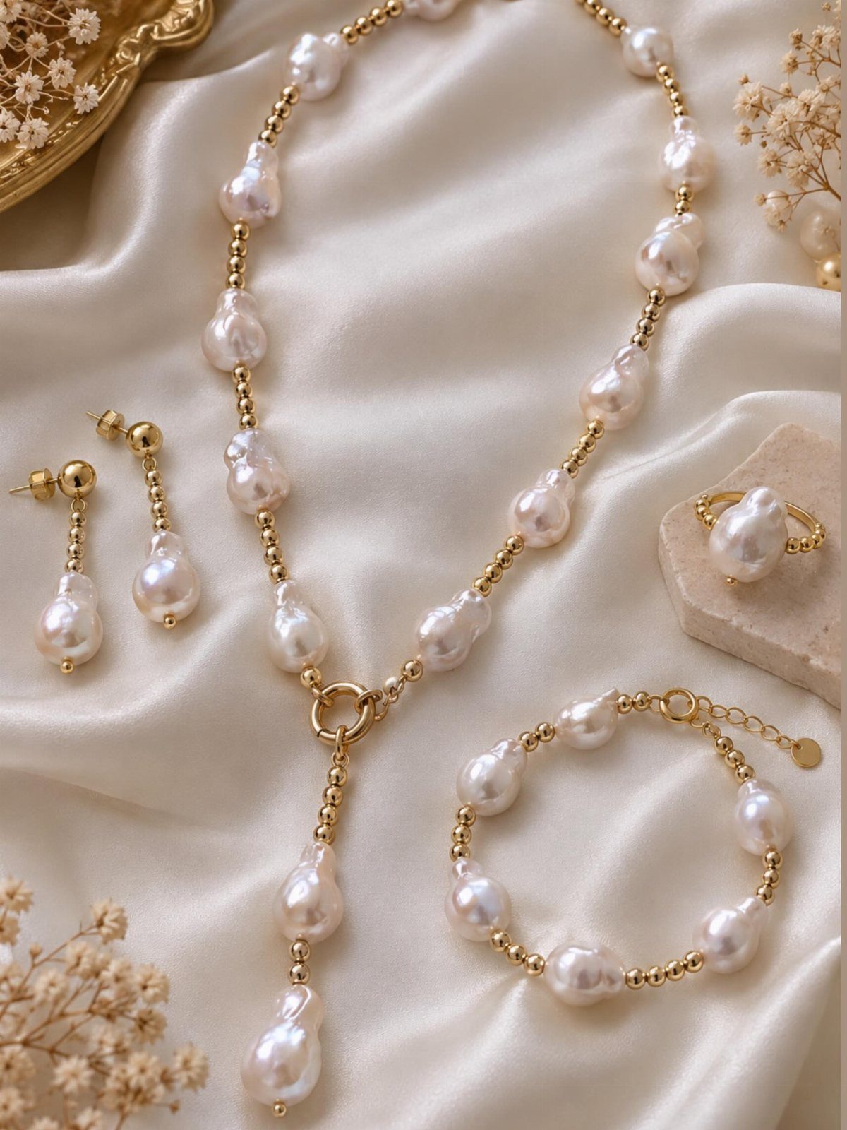 Baroque pearl jewelry set with gold accents resting on cream satin fabric with dried flowers.