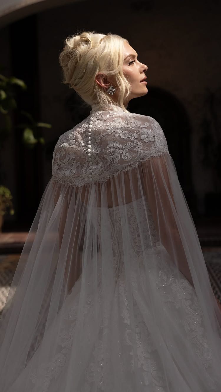 Blonde woman wearing an elegant white lace and sheer tulle bridal cape over a wedding dress.