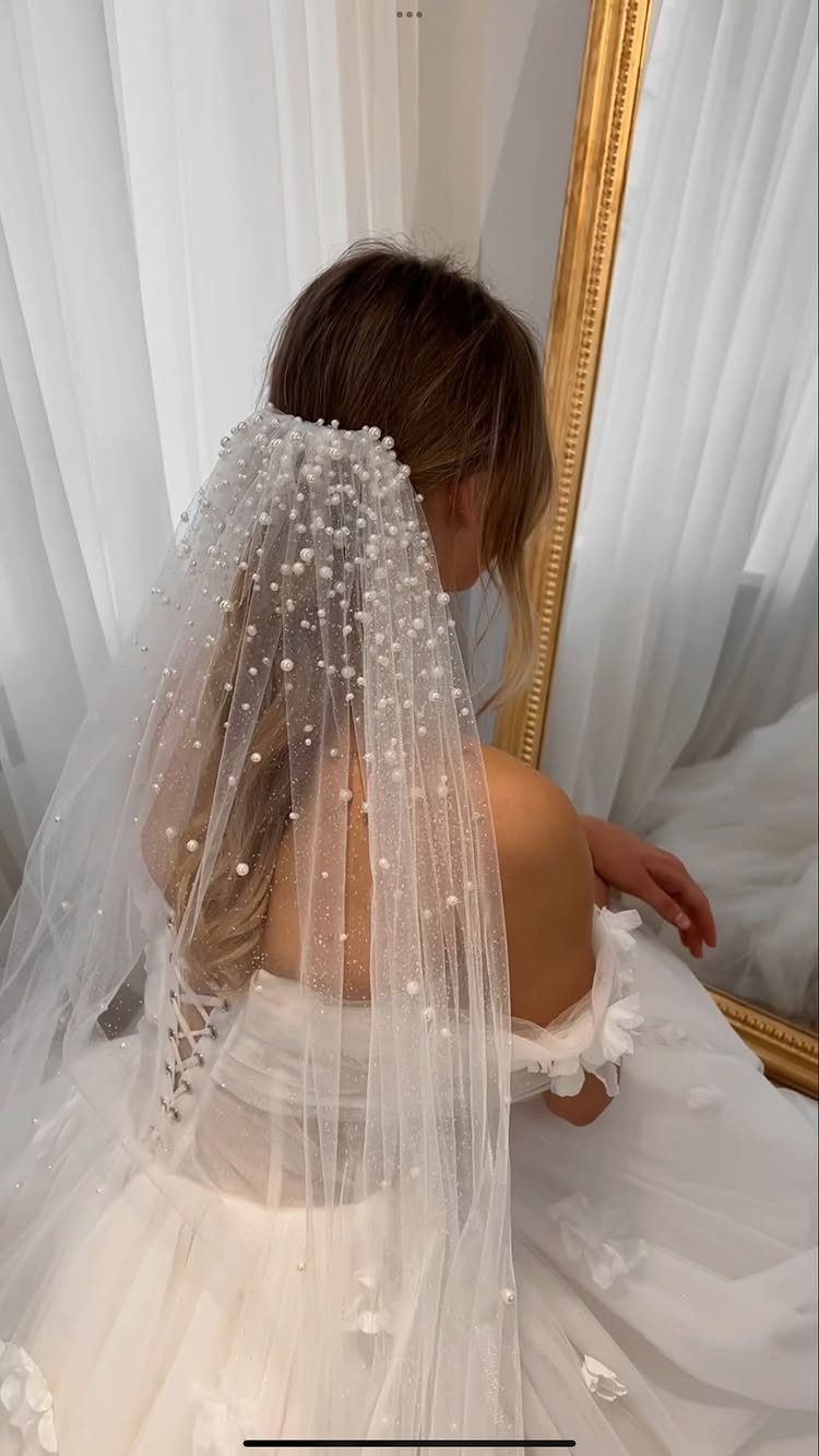 A woman wearing a white wedding dress and a pearl-adorned tulle veil.
