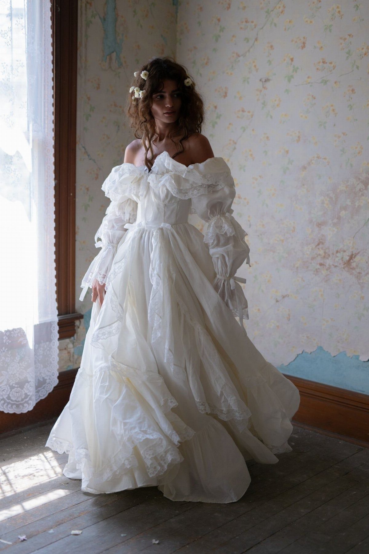 Wedding Dress Trends: 10 Looks for 2026 8 A woman in a white wedding dress with large, billowy sleeves standing in a sunlit room.