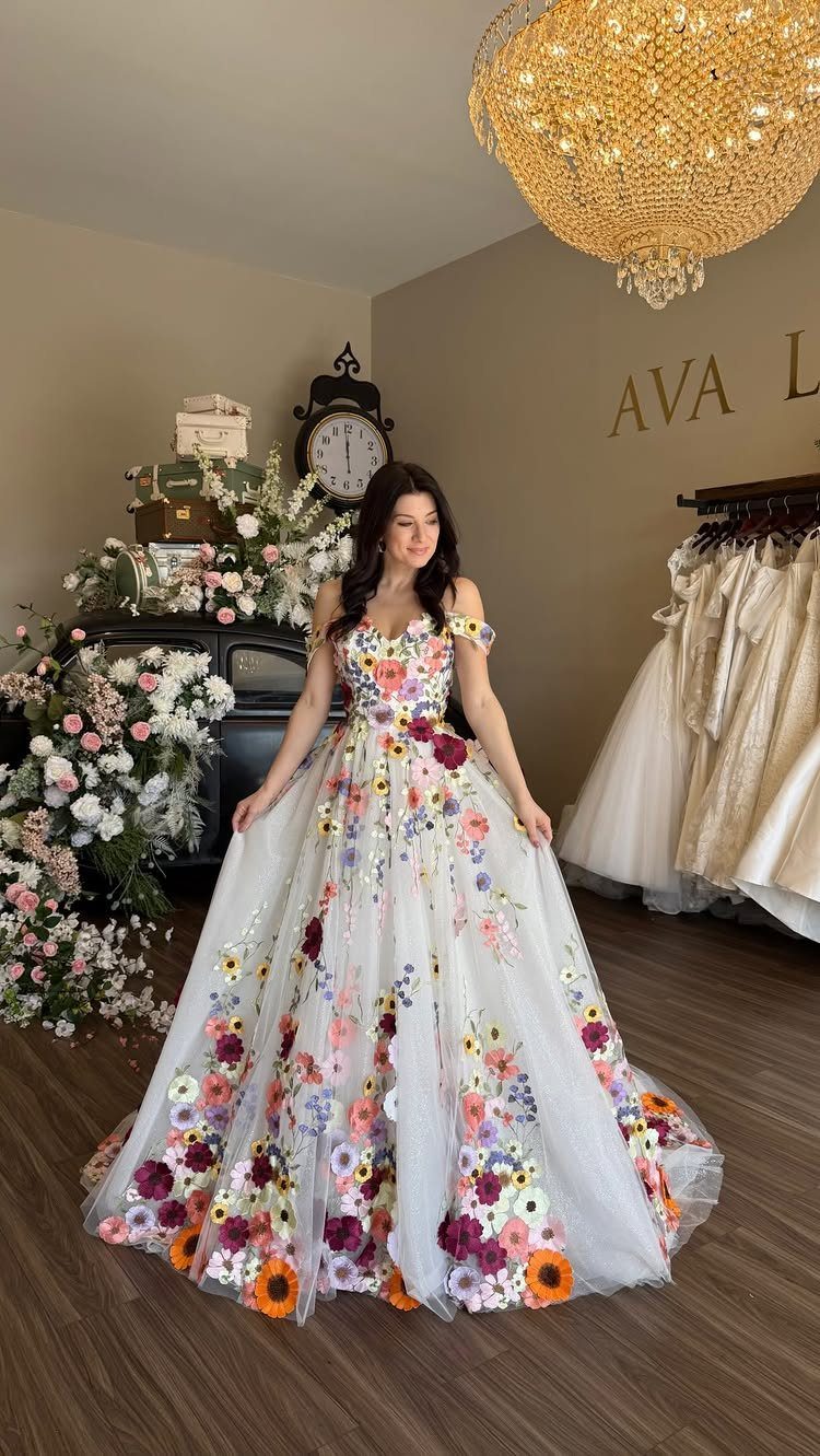 Wedding Dress Trends: 10 Looks for 2026 3 A woman wearing a white wedding dress adorned with vibrant, colorful 3D floral appliques.