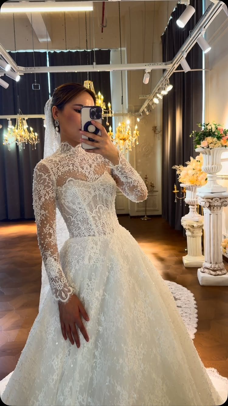 Wedding Dress Trends: 10 Looks for 2026 7 A woman in a white lace wedding dress with long sleeves posing for a mirror selfie.