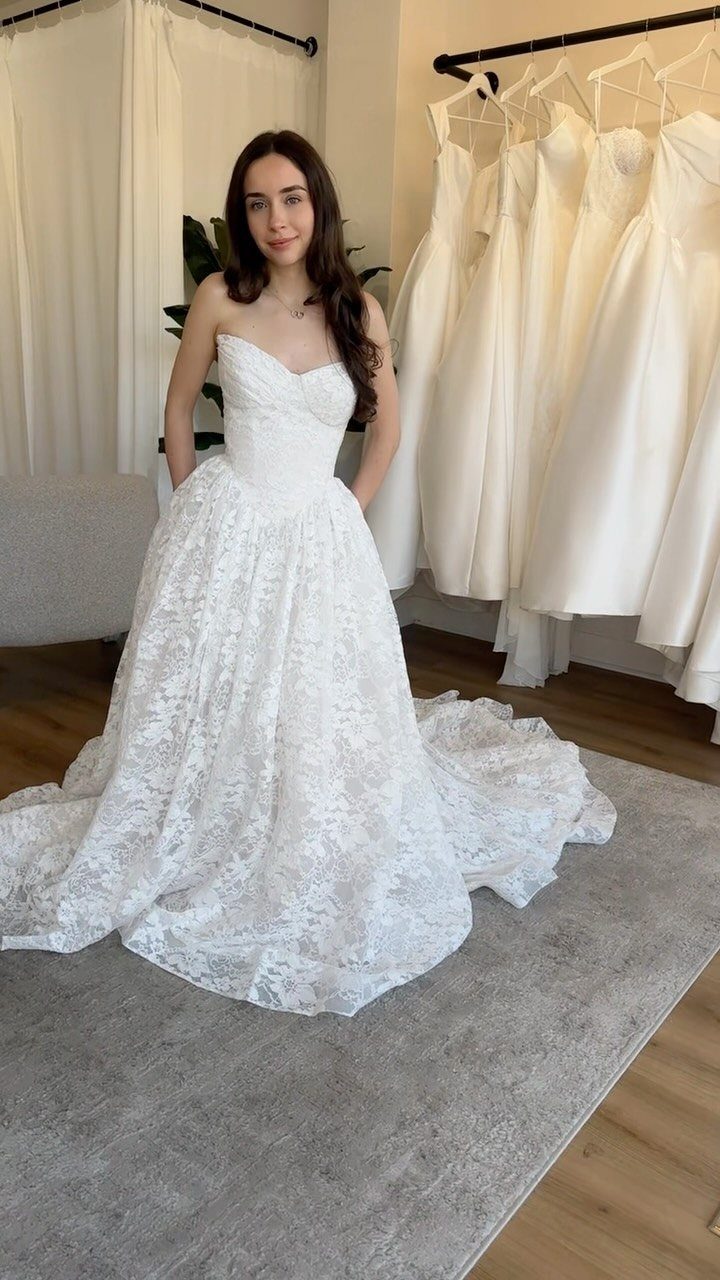 5 Wedding Dress with Bodice Ideas from Corset Gowns to Draped Satin 4 Woman wearing a strapless white lace wedding gown standing in a bridal boutique.