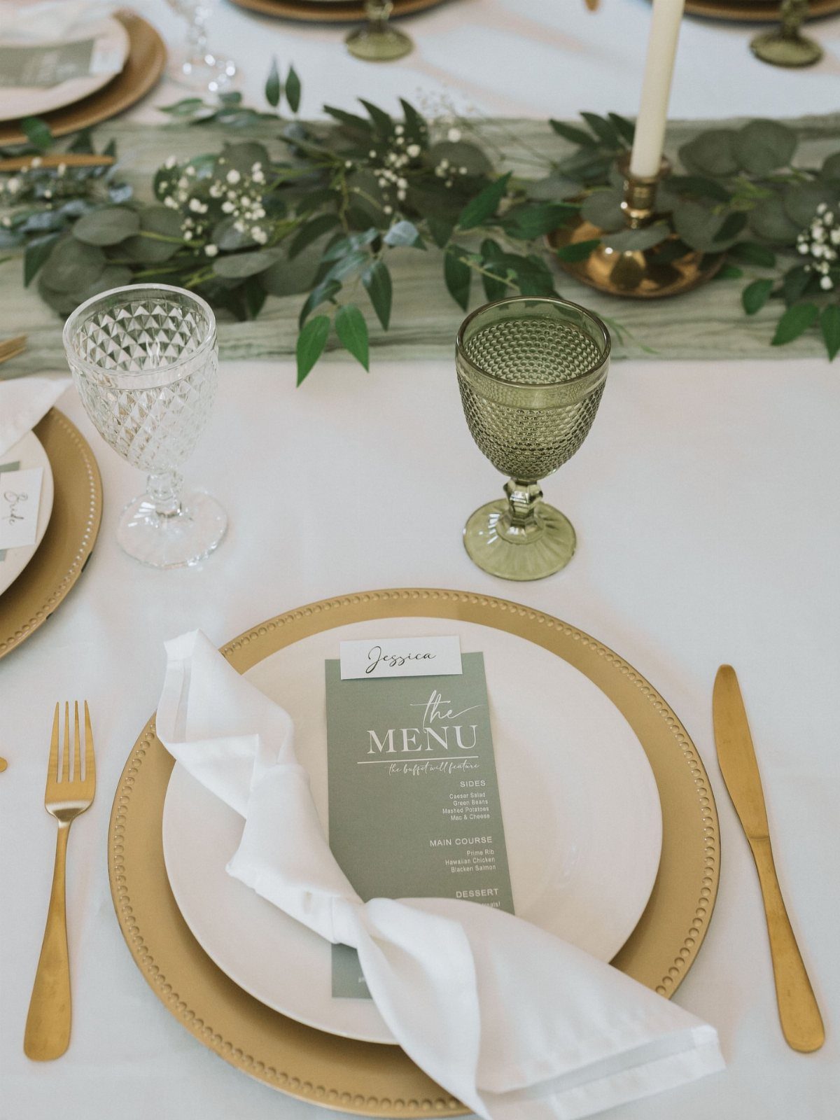 A formal wedding table setting with gold chargers, white plates, green menus, and eucalyptus greenery.