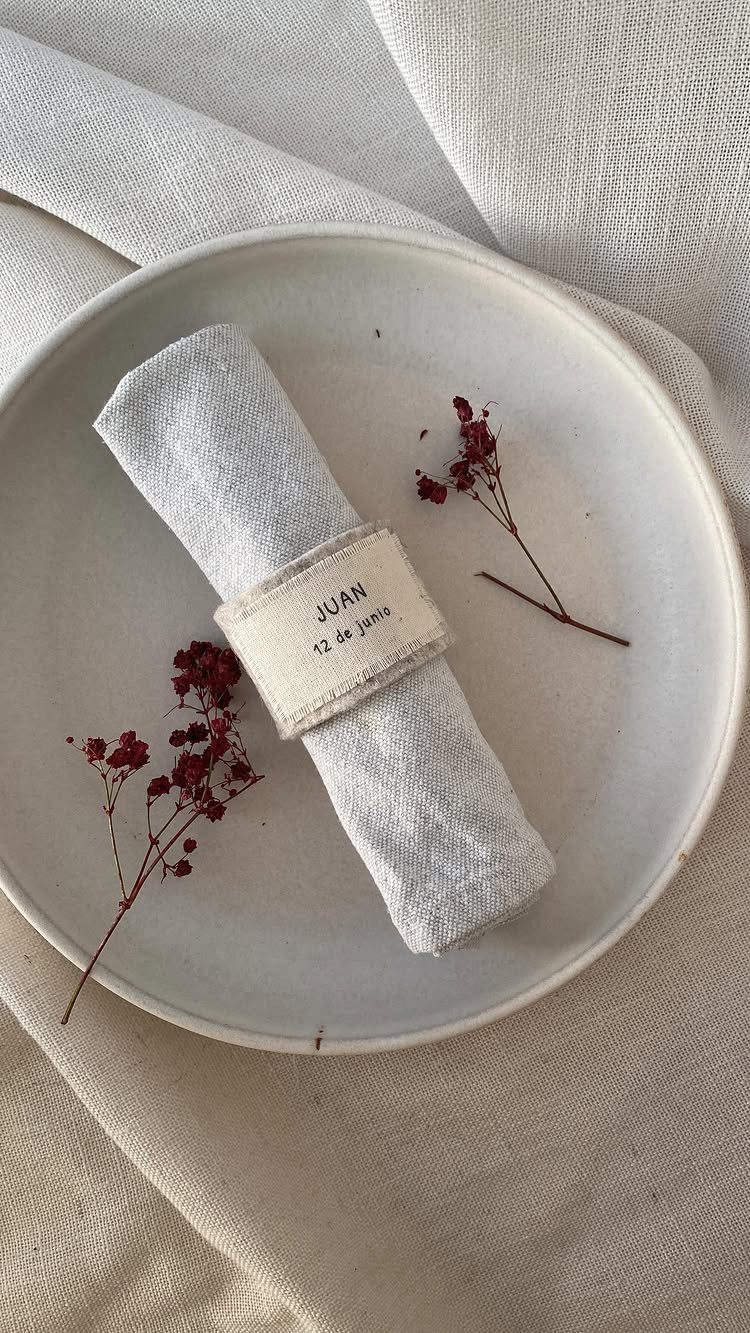 A light grey plate with a rolled blue napkin and dried red flowers on white linen.