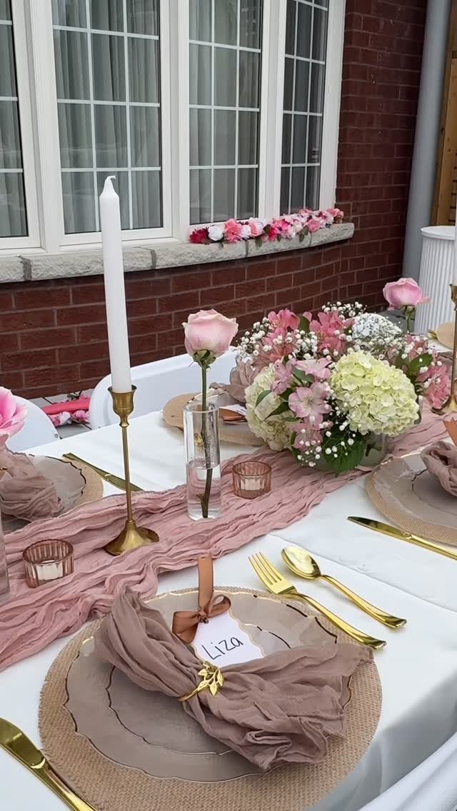 A romantic wedding table setting with pink flowers, gold cutlery, and a dusty rose runner.
