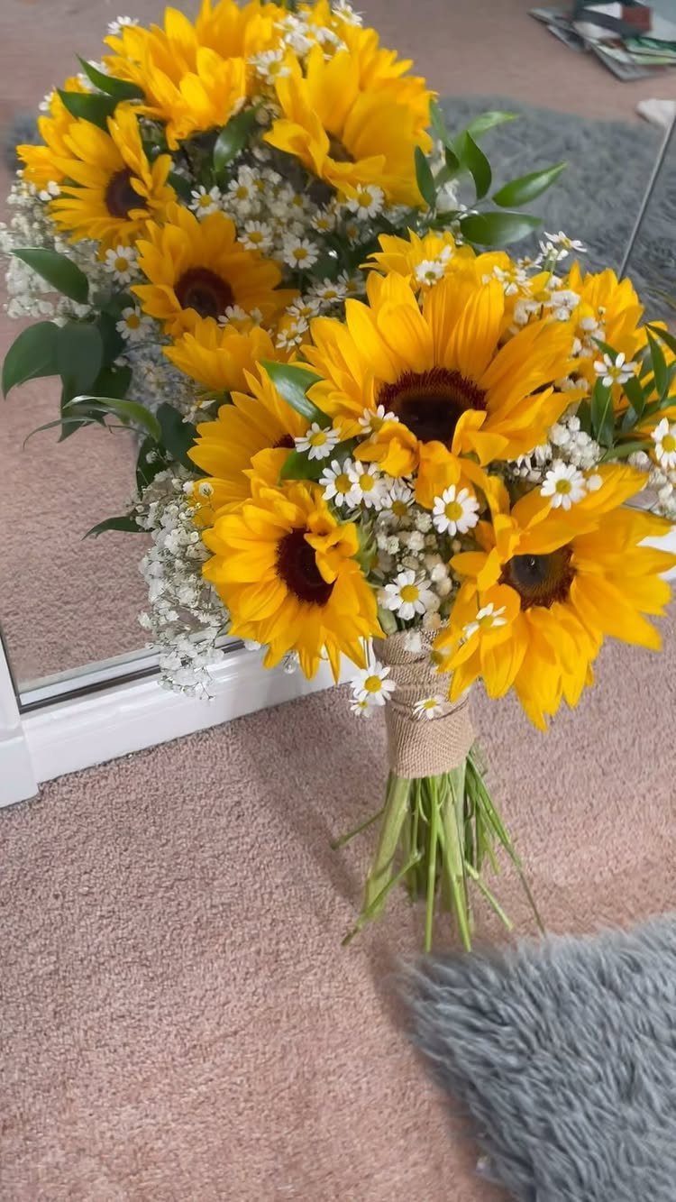 A vibrant sunflower bouquet with white daisies and green leaves tied with burlap ribbon.