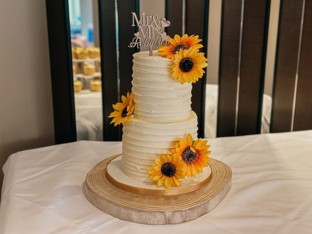 A two-tier white wedding cake decorated with vibrant sunflowers and a Mr and Mrs topper.