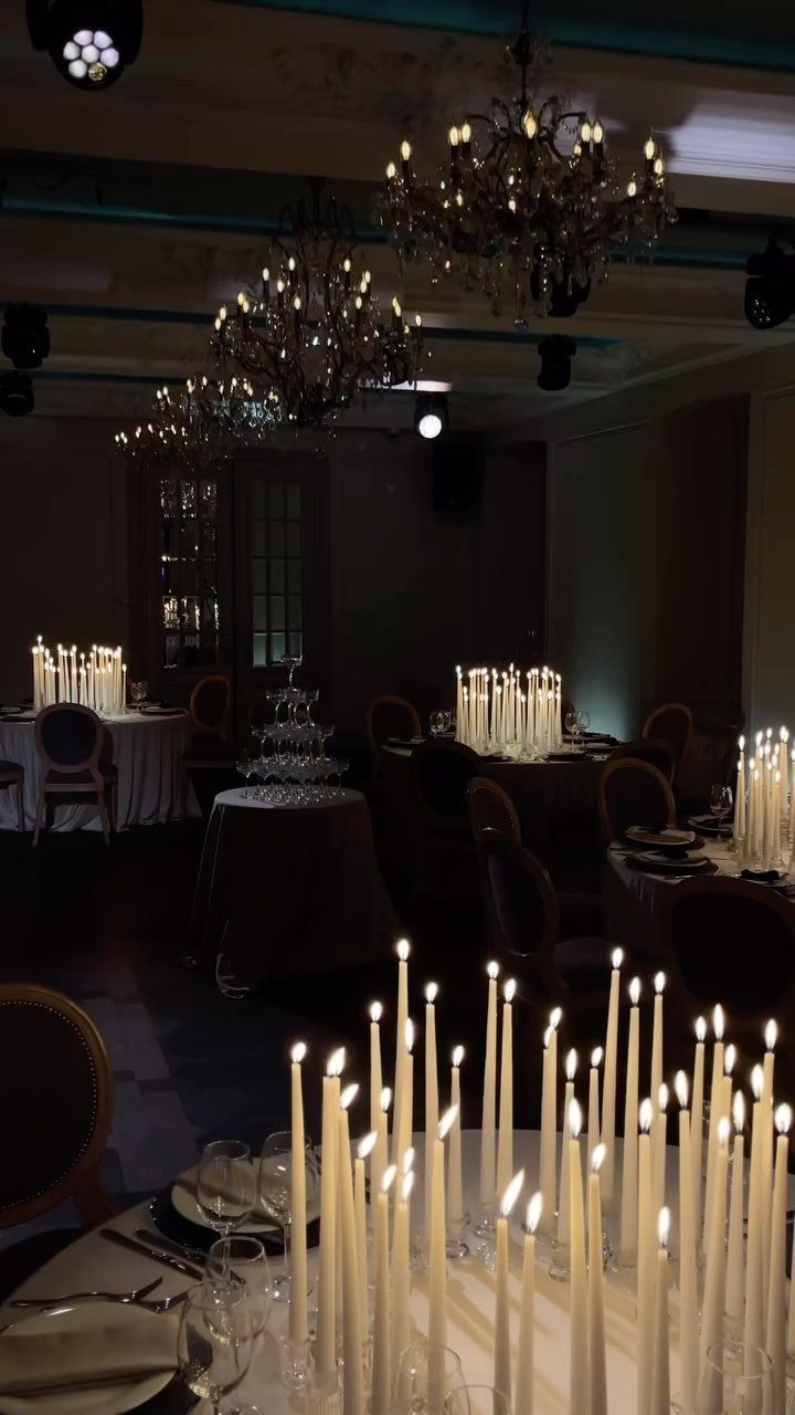 10 Wedding Themes Winter Couples Will Love in 2026 4 Tall white taper candles in glass holders arranged on tables in a dimly lit ballroom.