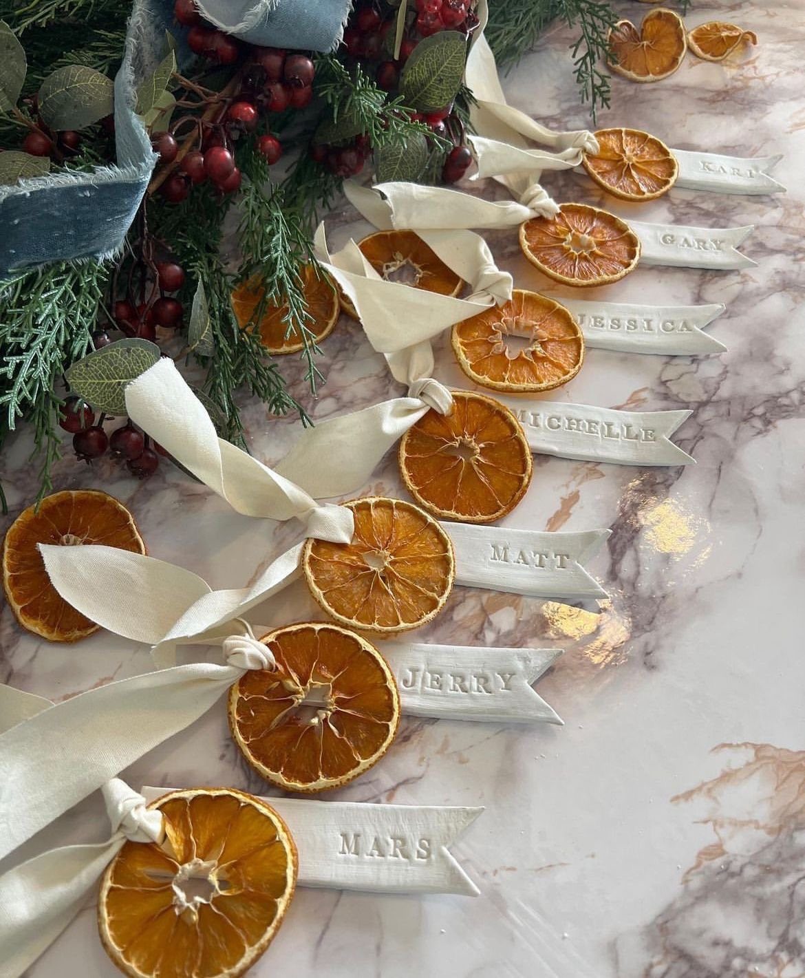 10 Wedding Themes Winter Couples Will Love in 2026 10 Dried orange slices with white name ribbons arranged on a marble surface with winter greenery.