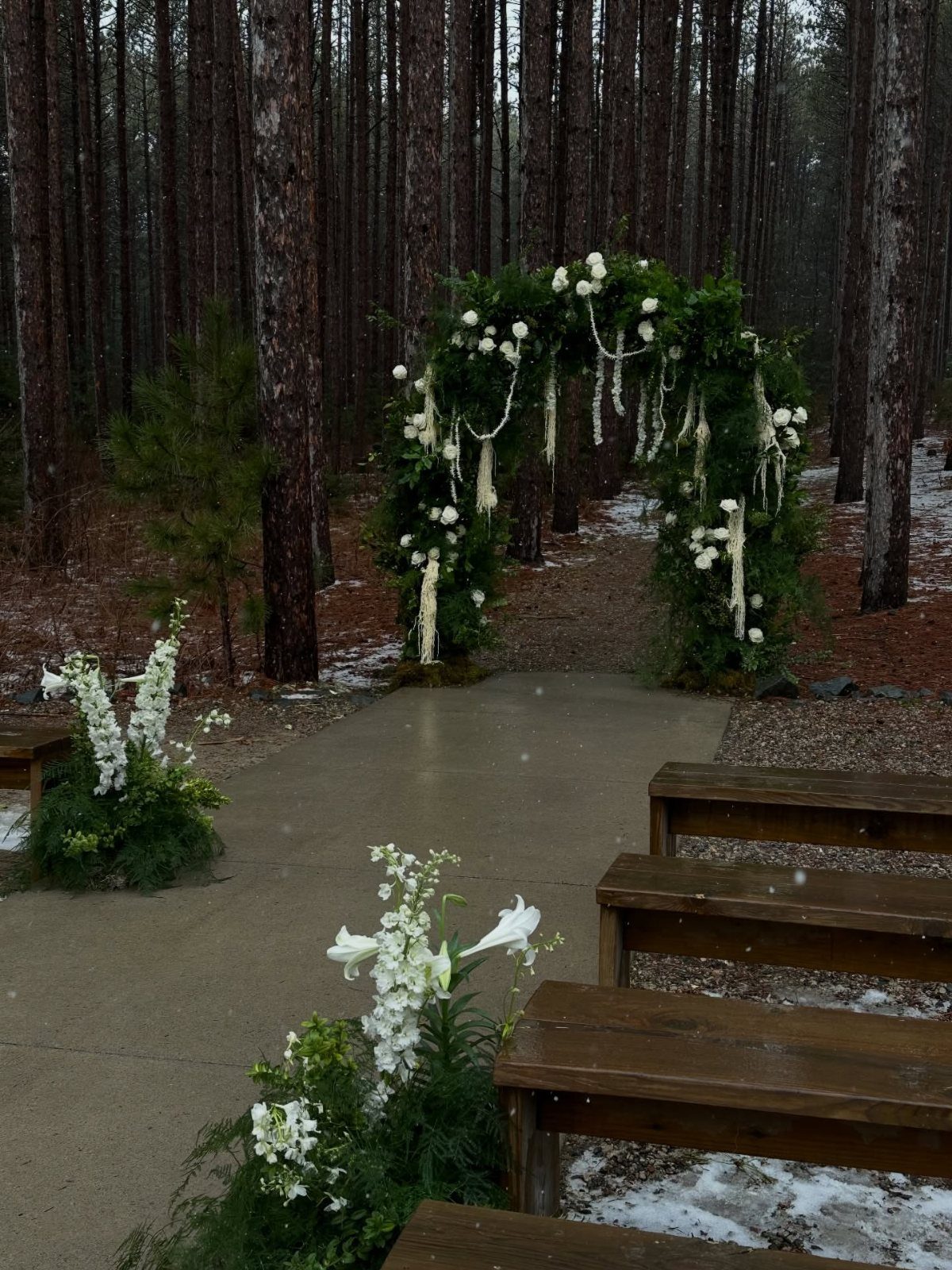 10 Wedding Themes Winter Couples Will Love in 2026 8 A green wedding arch with white flowers and garlands in a snowy pine forest.