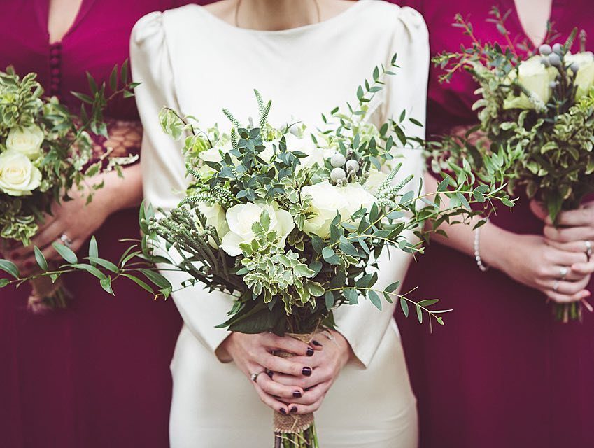 10 Wedding Themes Winter Couples Will Love in 2026 3 Three women holding winter wedding bouquets with white roses and green foliage.