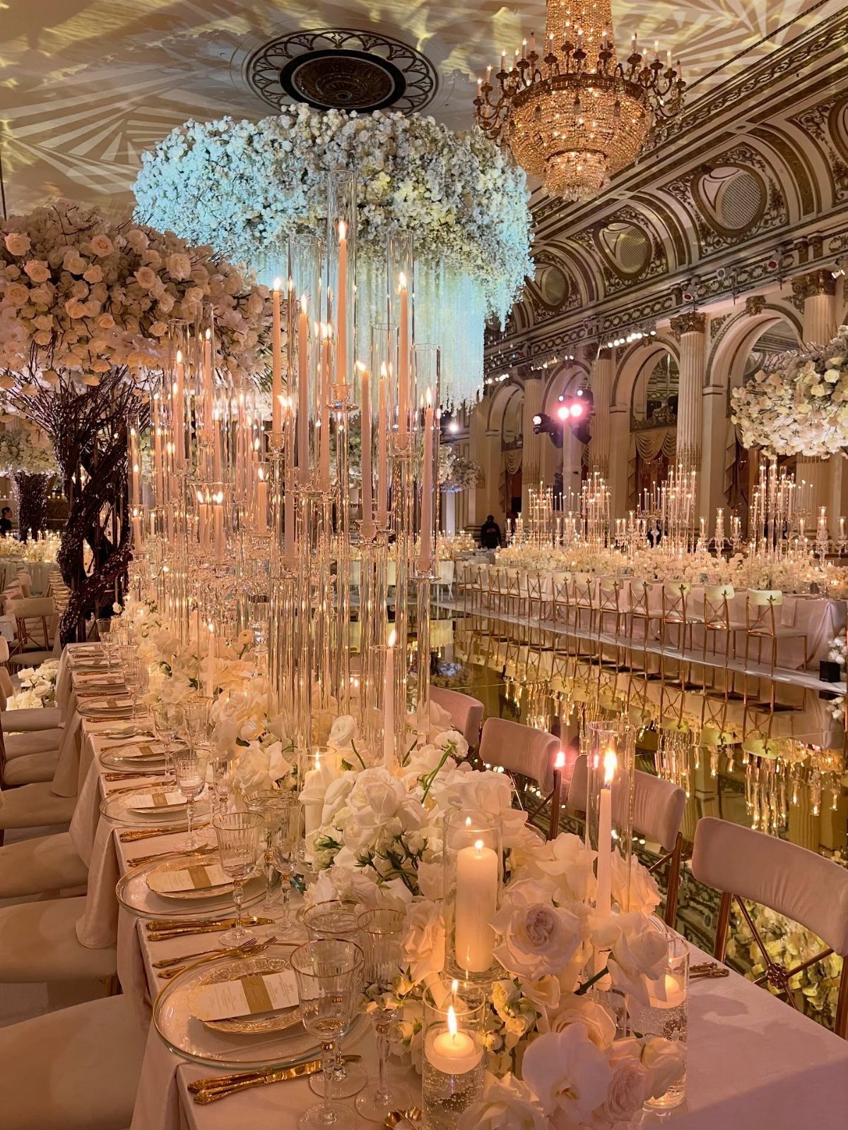 10 Wedding Themes Winter Couples Will Love in 2026 1 White floral centerpieces and tall candles decorate long banquet tables in a grand ballroom.