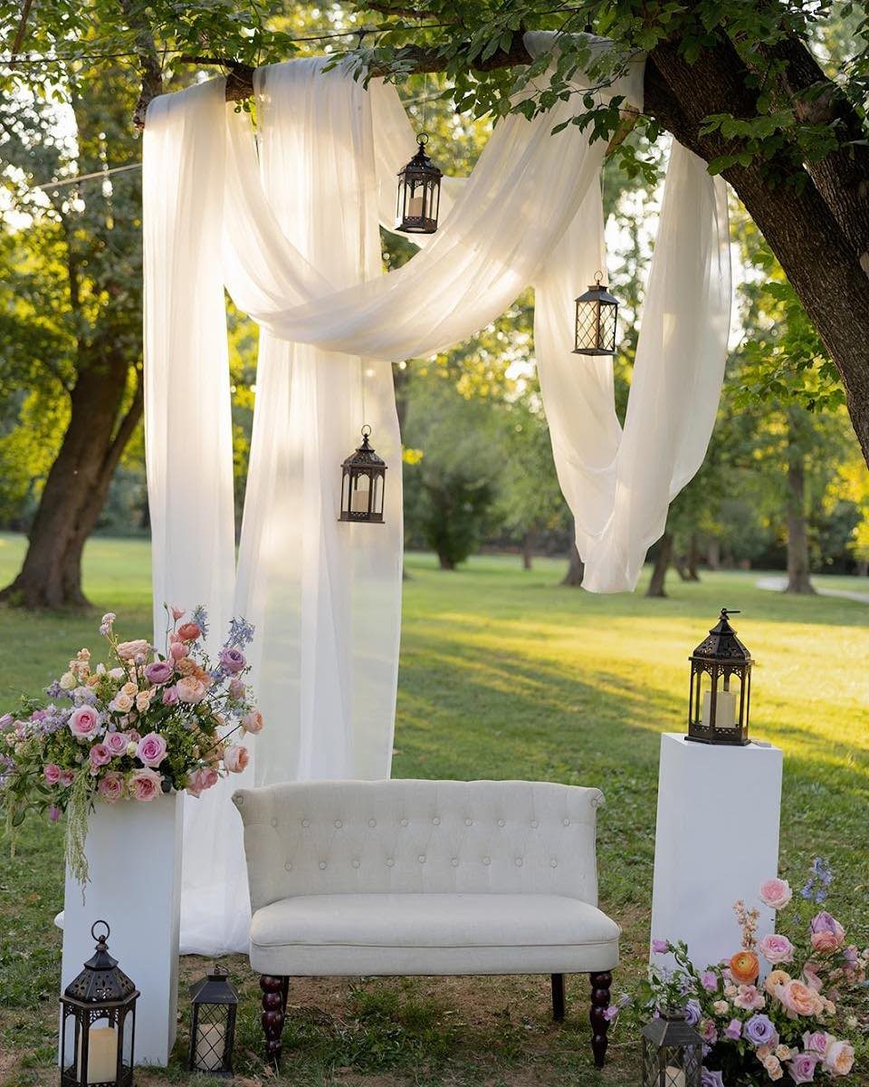 7 Wedding Tree Decorations That Work Outside the Ballroom 7 White fabric drapes and black lanterns hanging from a tree over a white loveseat.