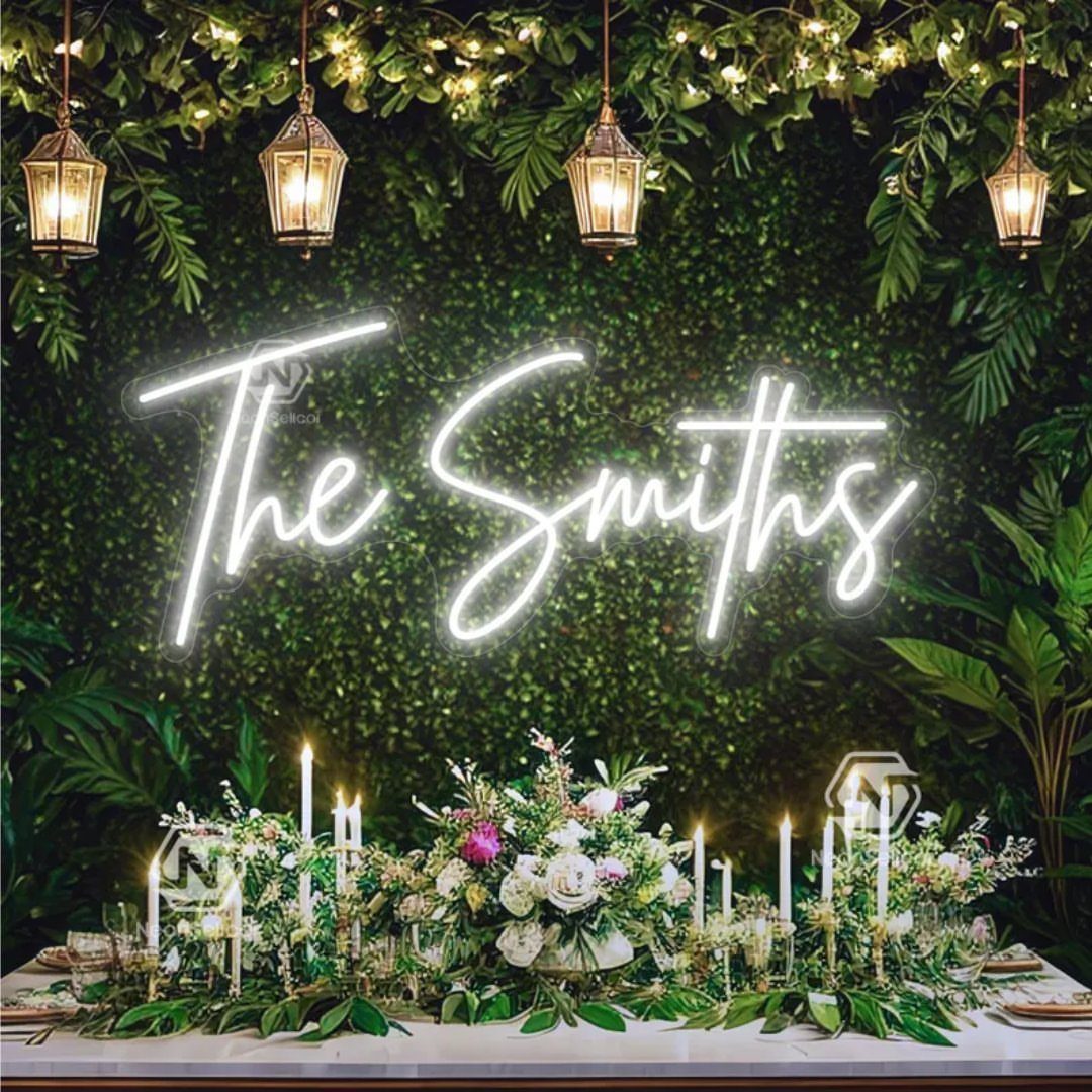 7 Wedding Tree Decorations That Work Outside the Ballroom 2 A white neon sign reading The Smiths against a green foliage wall above a decorated table.