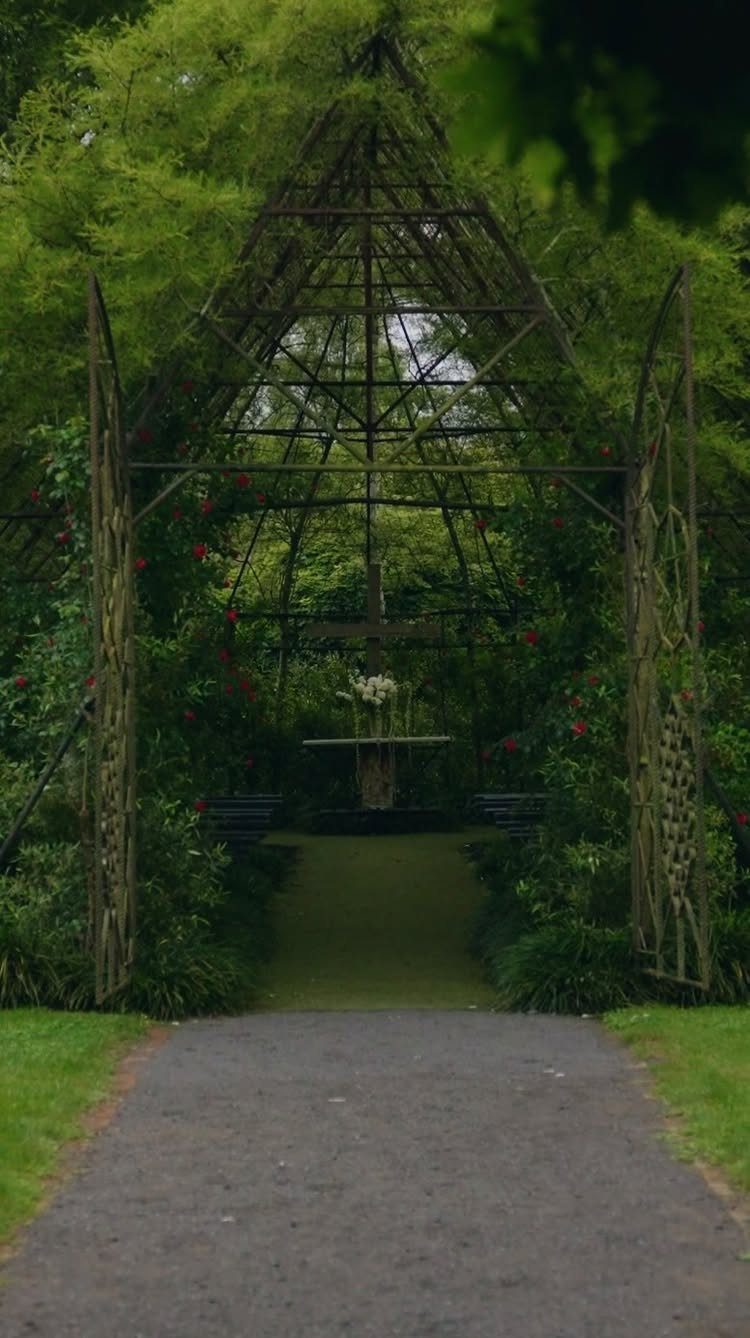 A tall metal trellis covered in green vines and red flowers framing a garden path.