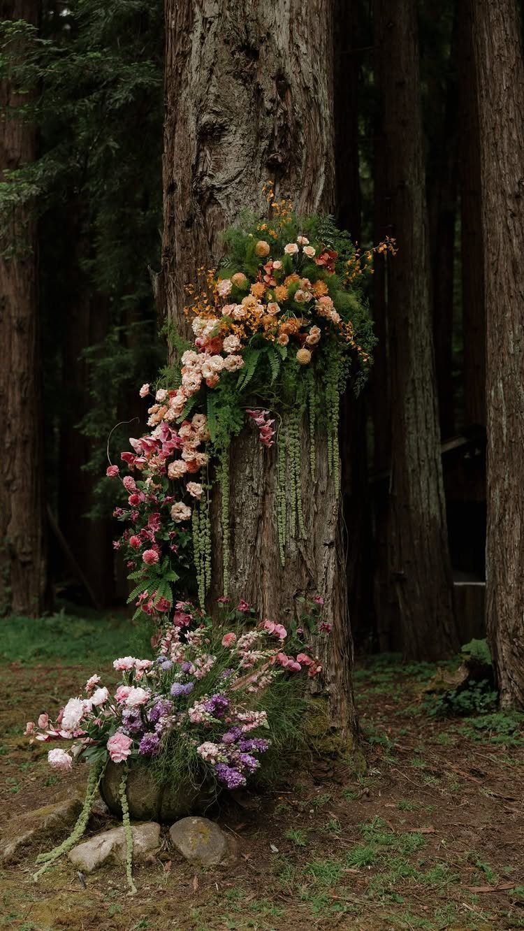 Colorful flowers cascading down a large tree trunk in a dark, wooded forest setting.