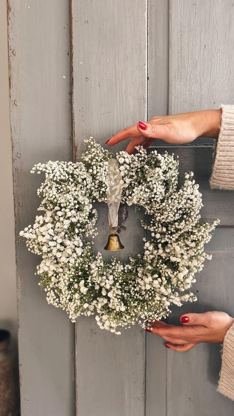19 Winter Wonderland Wedding Ideas for a Modern Celebration 19 Hands with red nail polish holding a white baby's breath wreath against a grey wooden door.