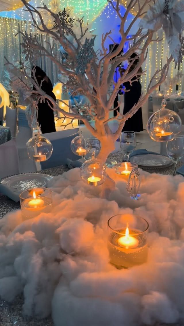 19 Winter Wonderland Wedding Ideas for a Modern Celebration 1 White decorative tree with hanging glass tea lights amidst fluffy white snow-like material and glowing candles.
