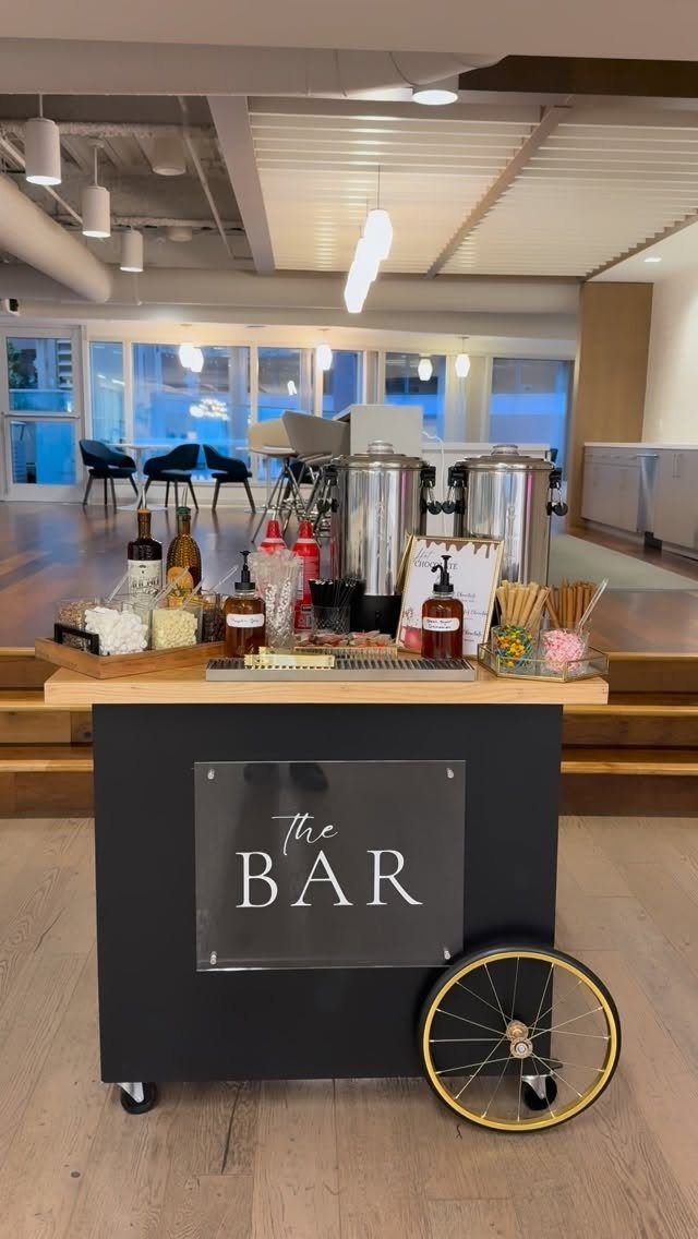 19 Winter Wonderland Wedding Ideas for a Modern Celebration 14 A black mobile beverage bar cart with silver dispensers and various drink toppings.