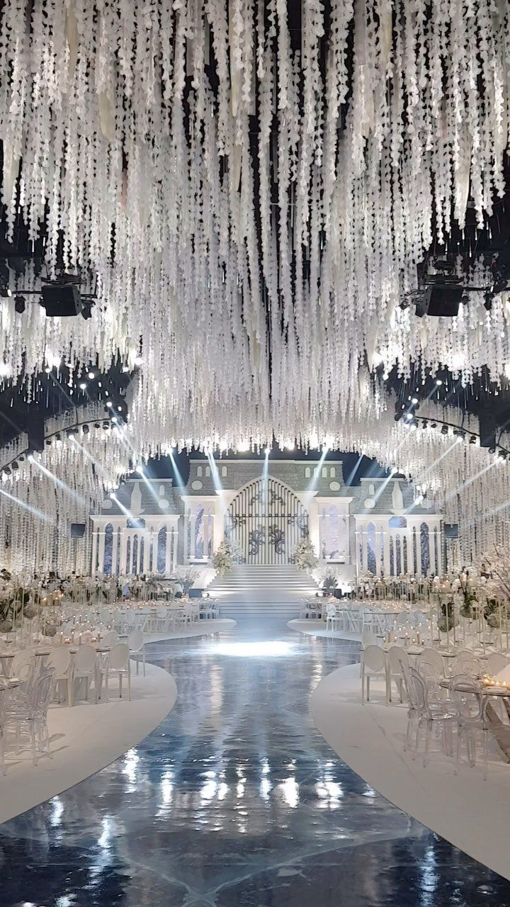 19 Winter Wonderland Wedding Ideas for a Modern Celebration 17 A grand wedding hall decorated with hanging white floral strands and a reflective blue ice-like aisle.
