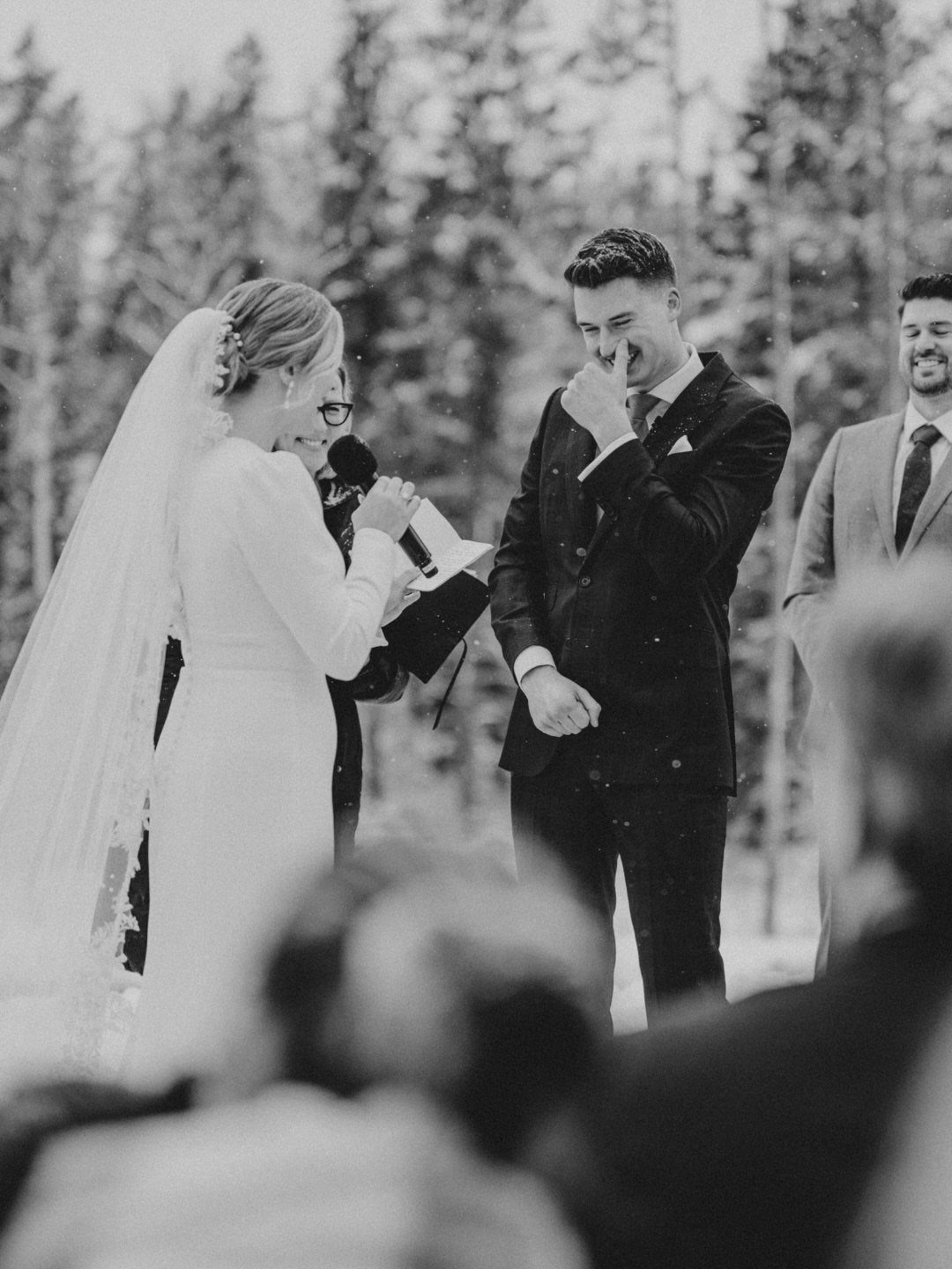 19 Winter Wonderland Wedding Ideas for a Modern Celebration 13 A bride and groom exchange vows during an outdoor wedding ceremony in a snowy forest.