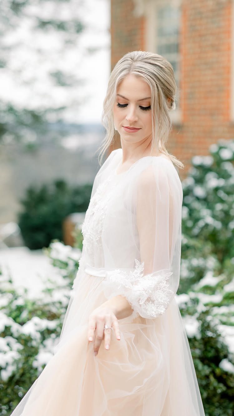 19 Winter Wonderland Wedding Ideas for a Modern Celebration 3 A blonde bride in a white lace dress posing amidst snow-covered green bushes.