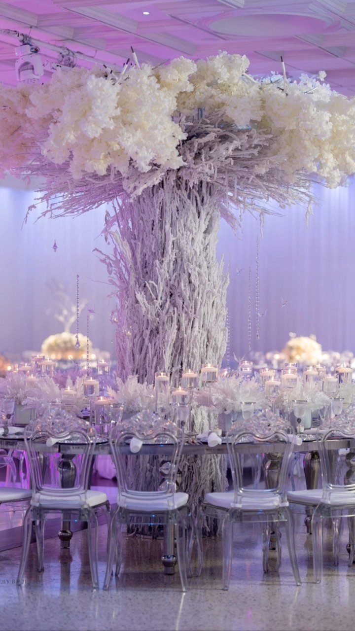 19 Winter Wonderland Wedding Ideas for a Modern Celebration 15 A large white floral tree centerpiece stands above a wedding reception table with clear chairs.